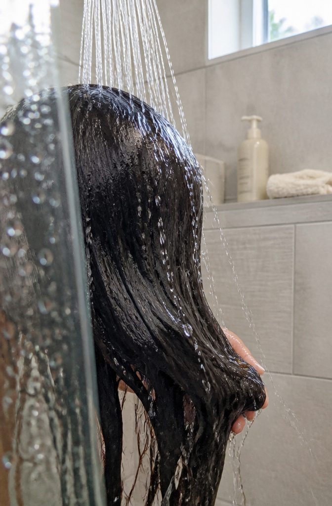 Cool shower water rinsing long dark hair above a basin
