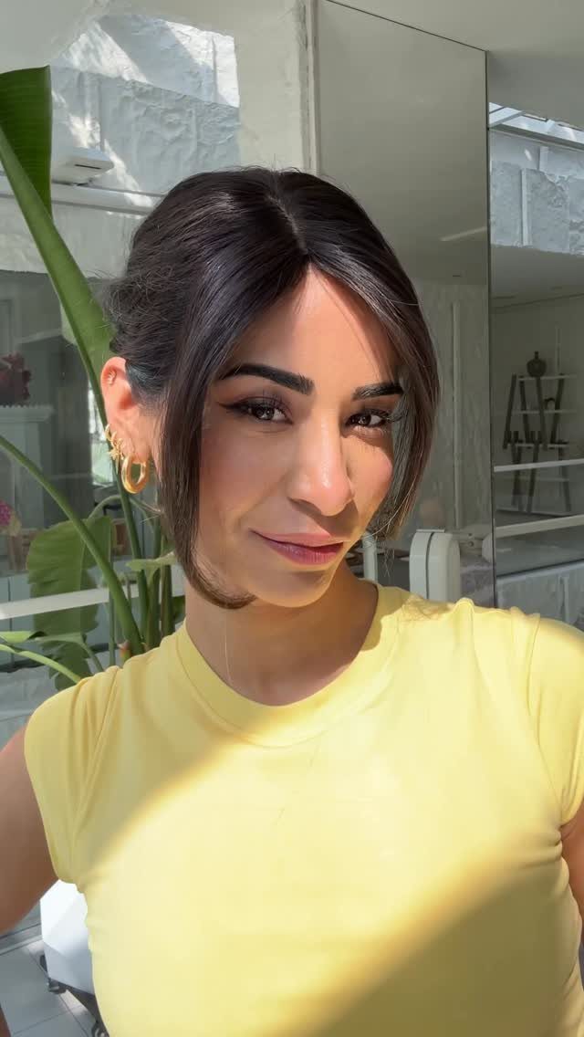 Woman with dark brown curtain bangs framing her face wearing a yellow shirt.