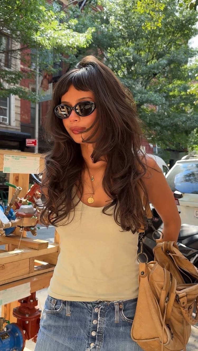 Woman with long wavy brown hair and a textured grunge fringe wearing sunglasses.