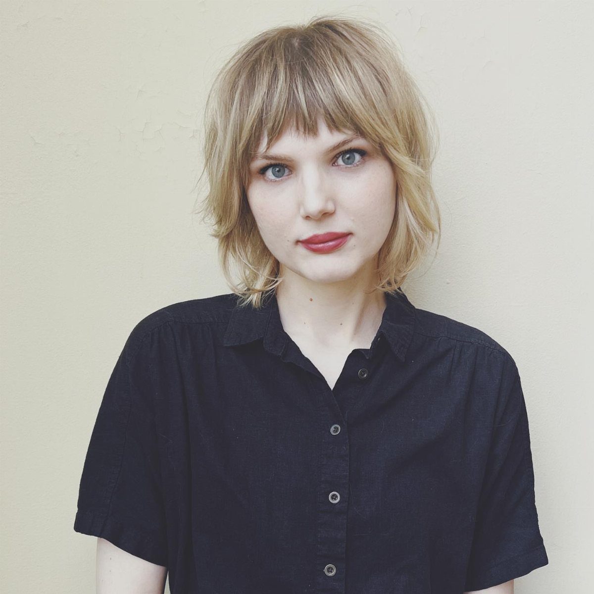 Woman with a blonde layered bob and full textured bangs wearing a black shirt.