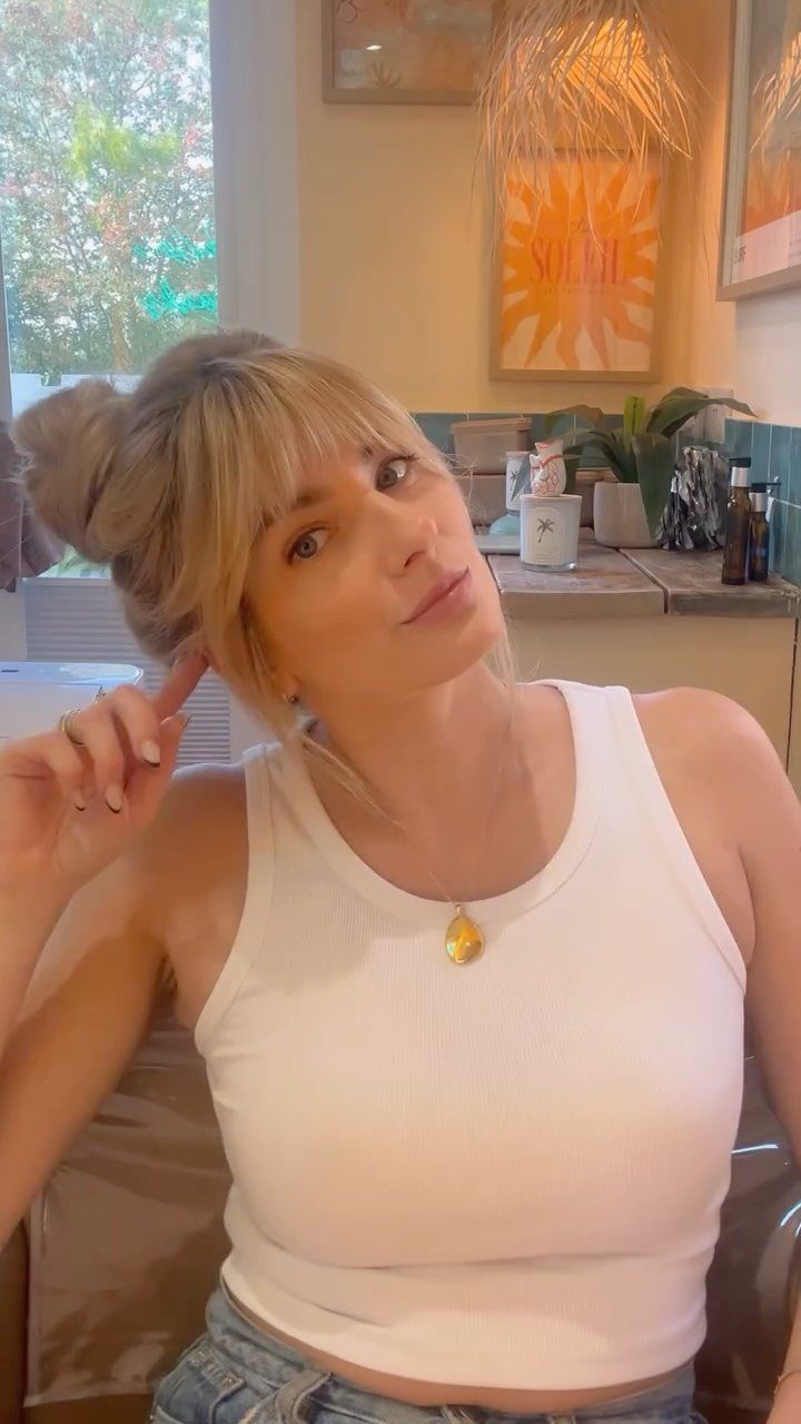 Woman with blonde hair and wispy bangs wearing a white sleeveless top.