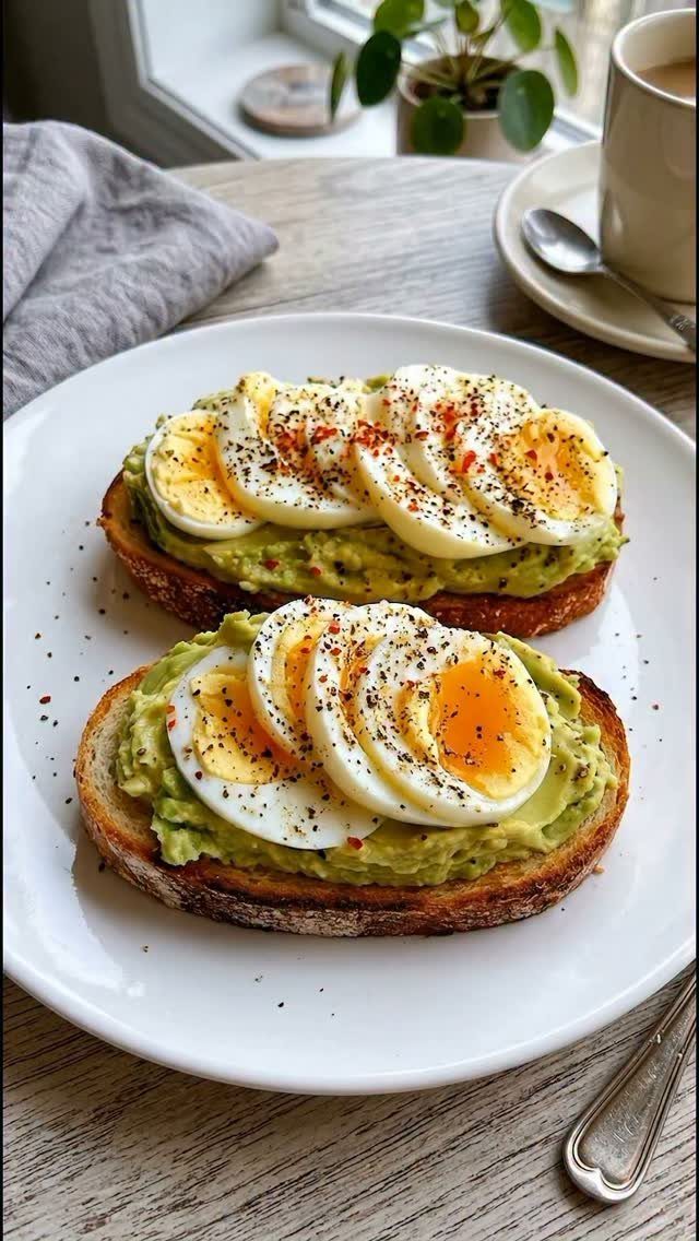 Avocado toast topped with sliced hard-boiled eggs on a white ceramic plate.