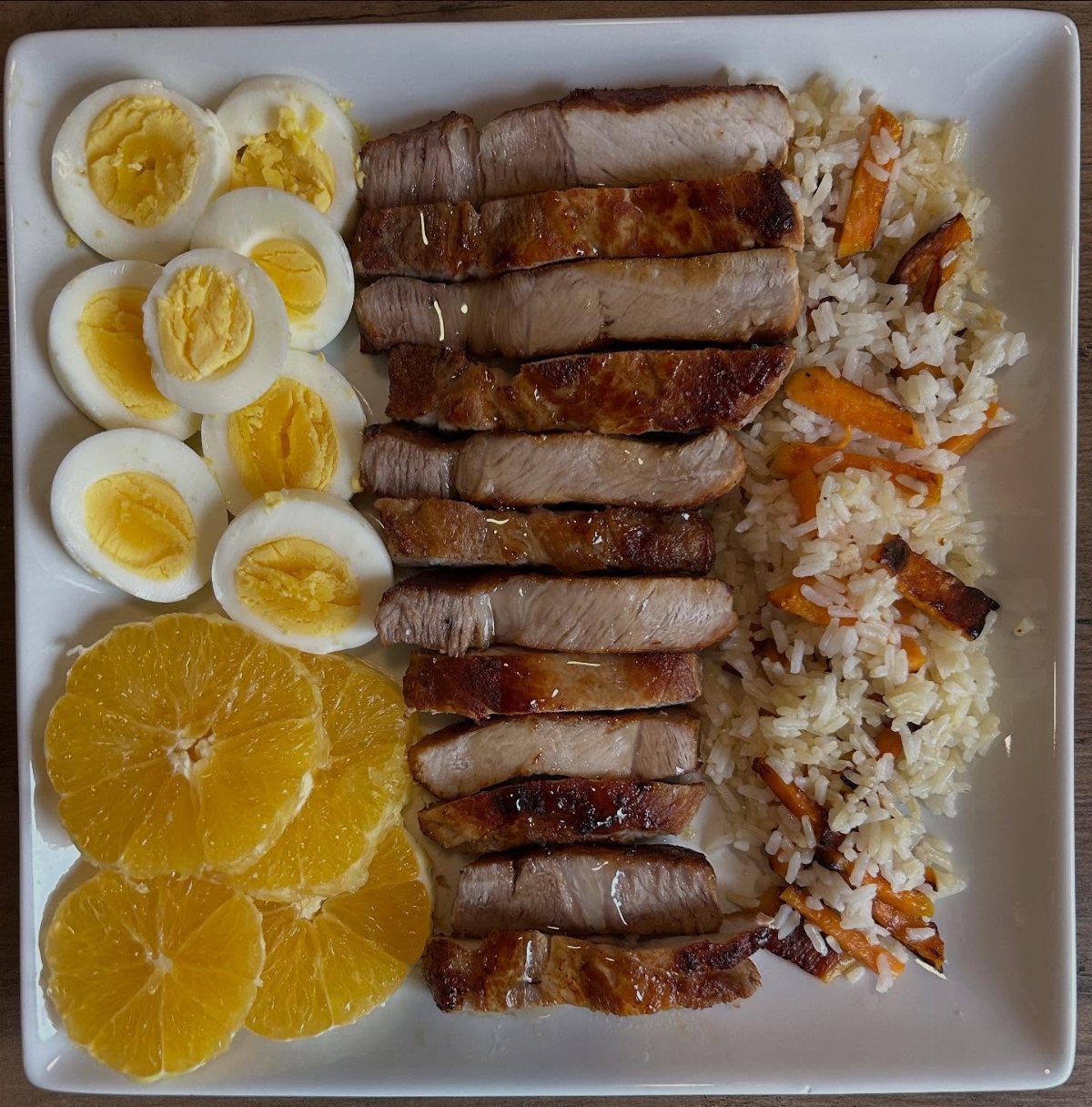 Platter of sliced eggs, grilled pork, rice with carrots, and orange slices.