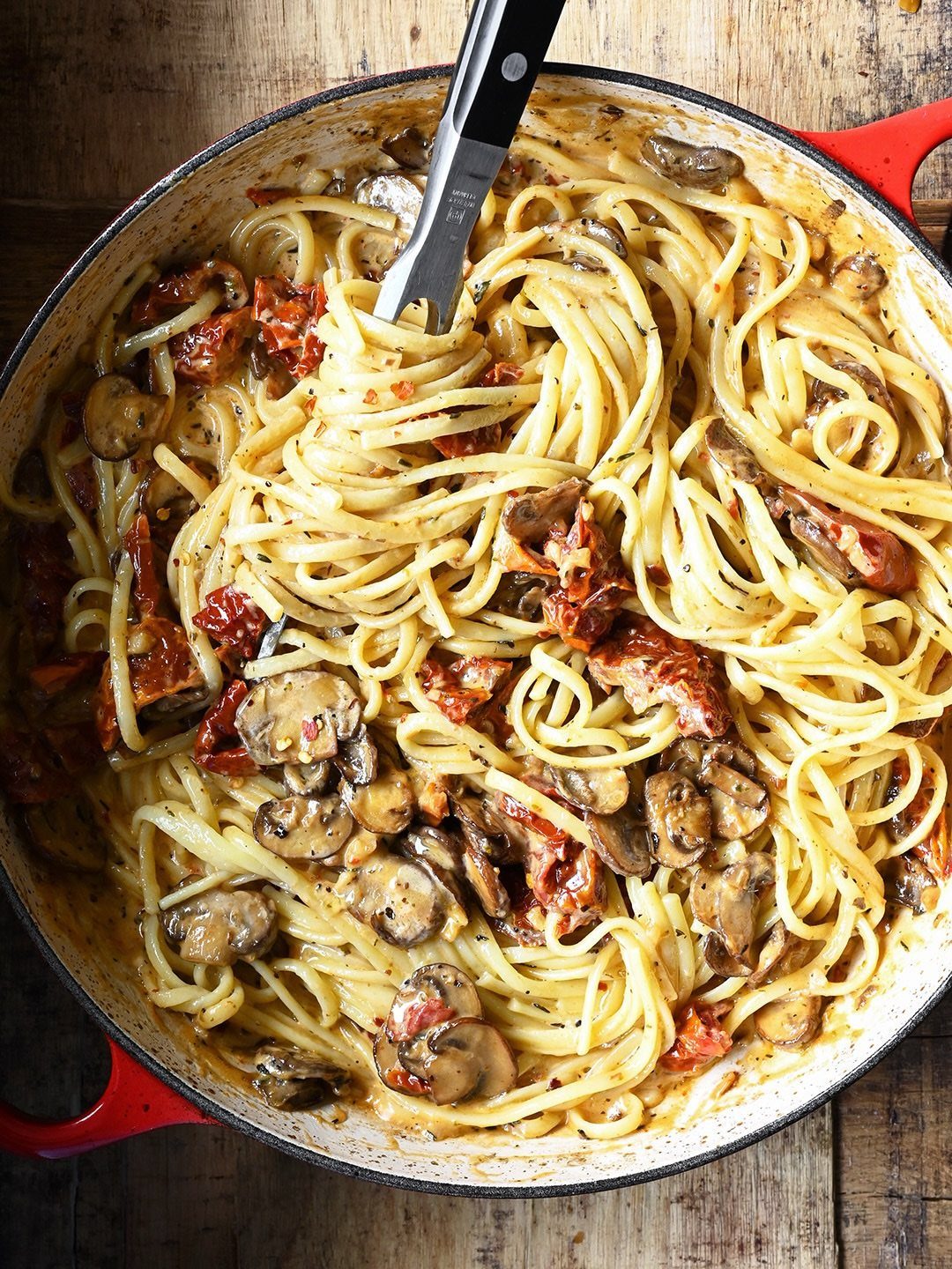 Creamy pasta with mushrooms and sun-dried tomatoes in a red cooking pot