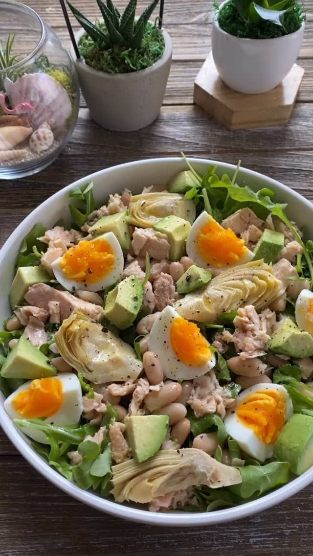 Salad bowl with eggs, avocado, tuna, and artichokes on a wooden table.