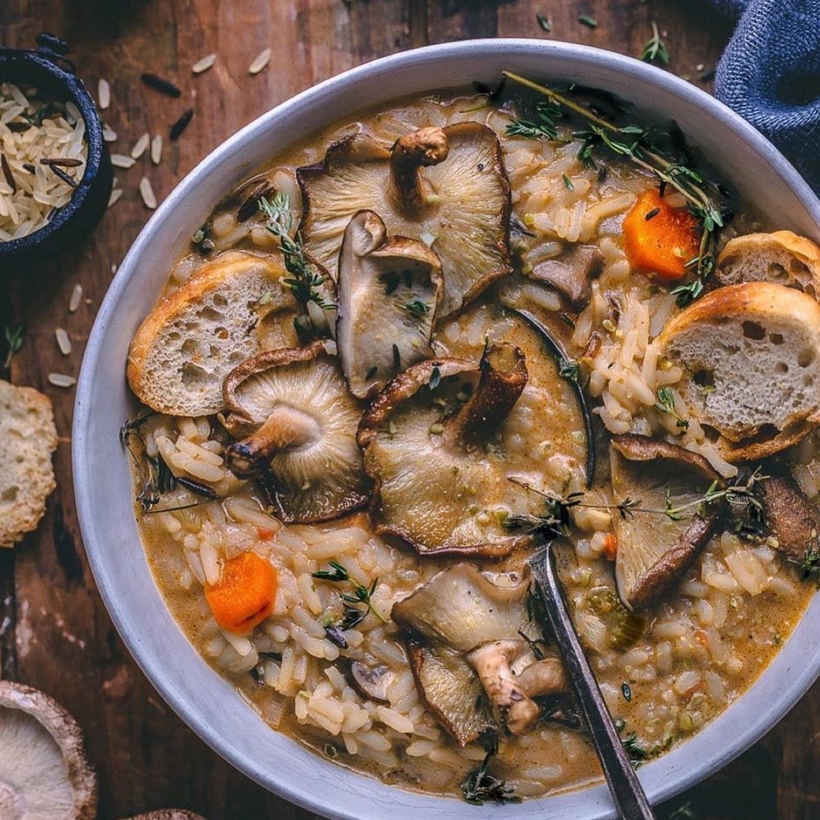 Creamy mushroom risotto with toasted bread and carrots in a grey bowl.
