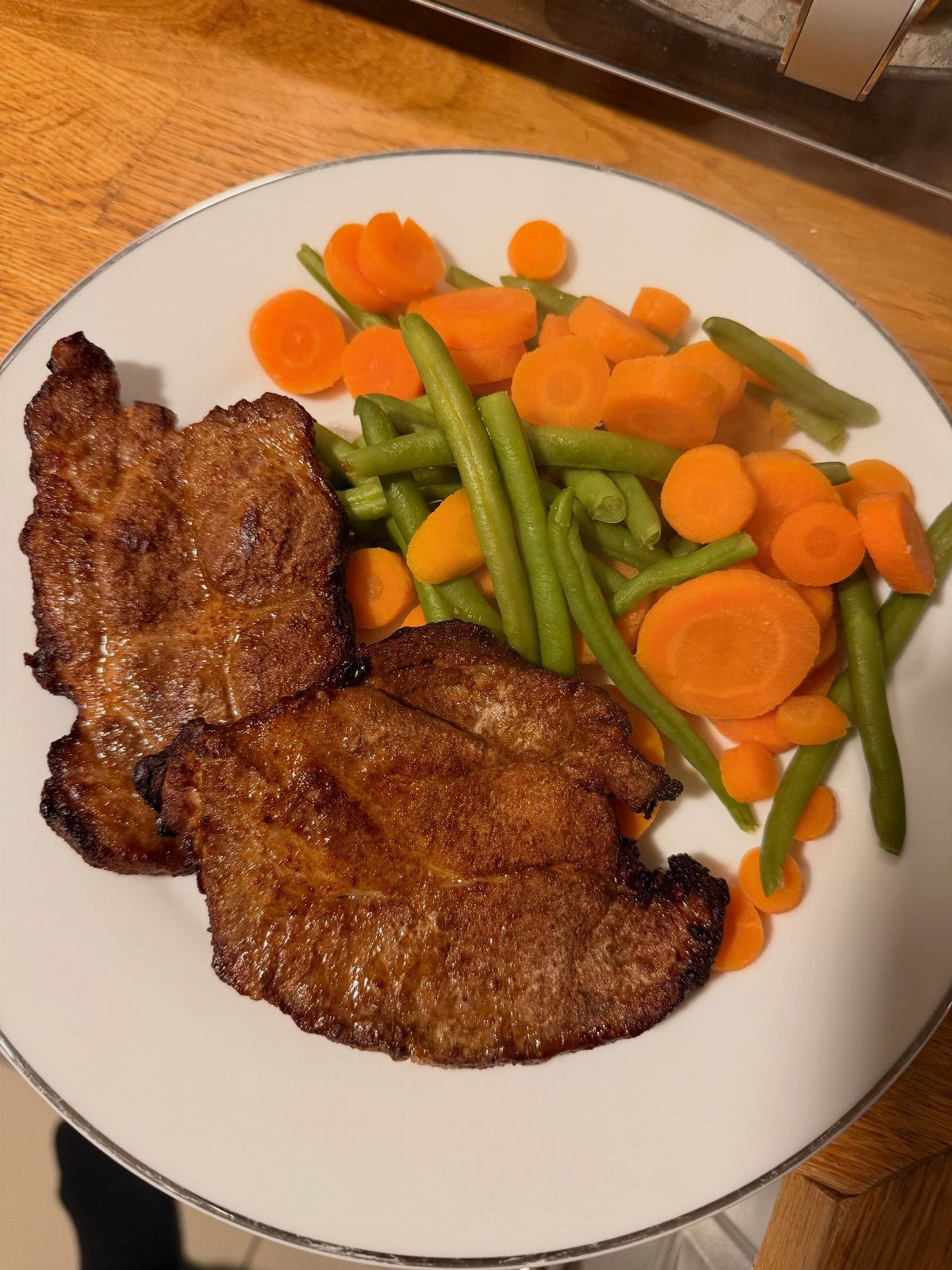 Two seared pork chops served with sliced carrots and green beans on a plate.