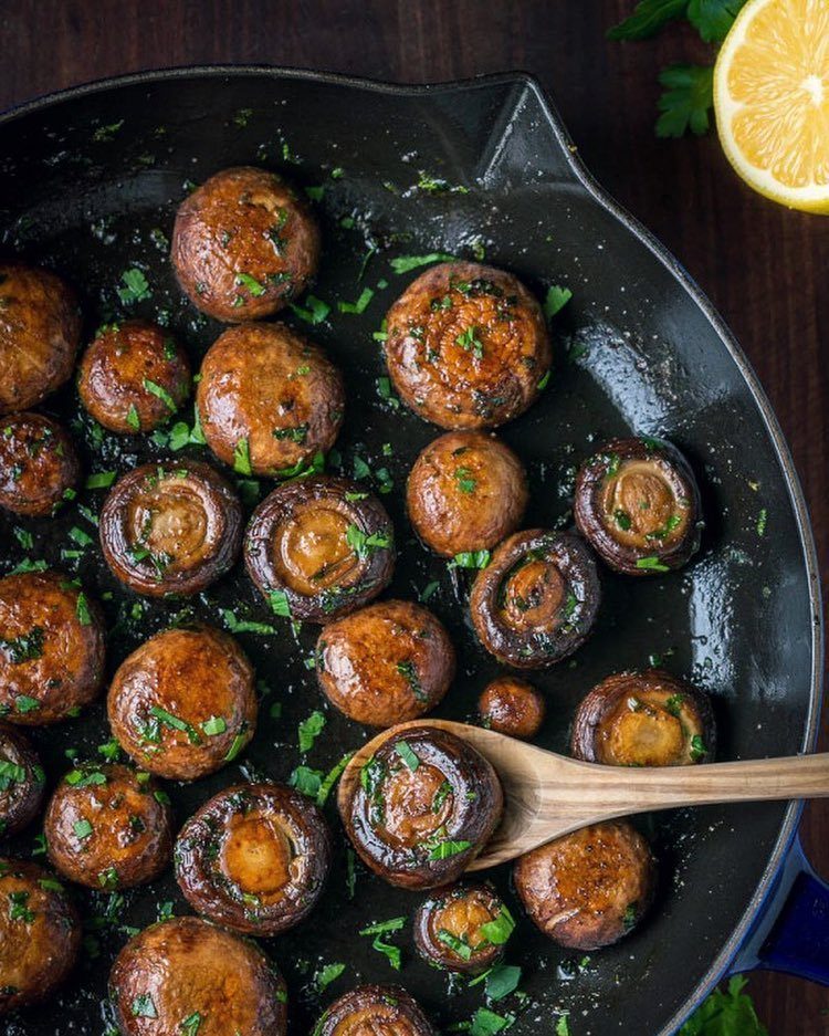 Sautéed brown mushrooms with fresh parsley in a black cast-iron skillet.
