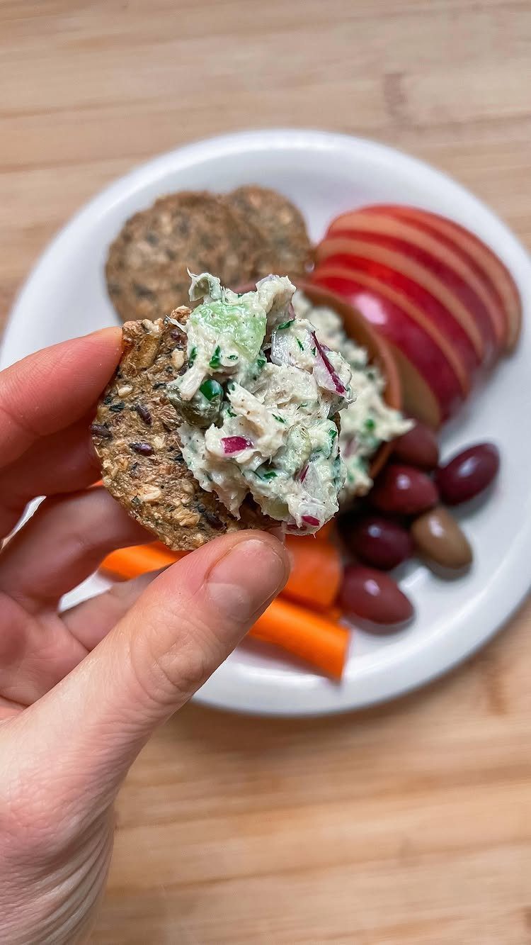Seed cracker with creamy herb salad, apples, carrots, and olives on a plate.