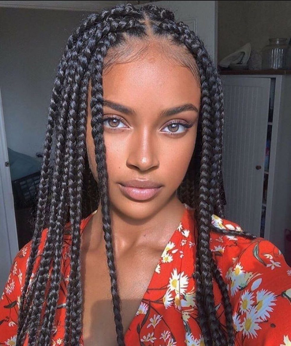 Woman with long black box braids wearing a red floral print dress.