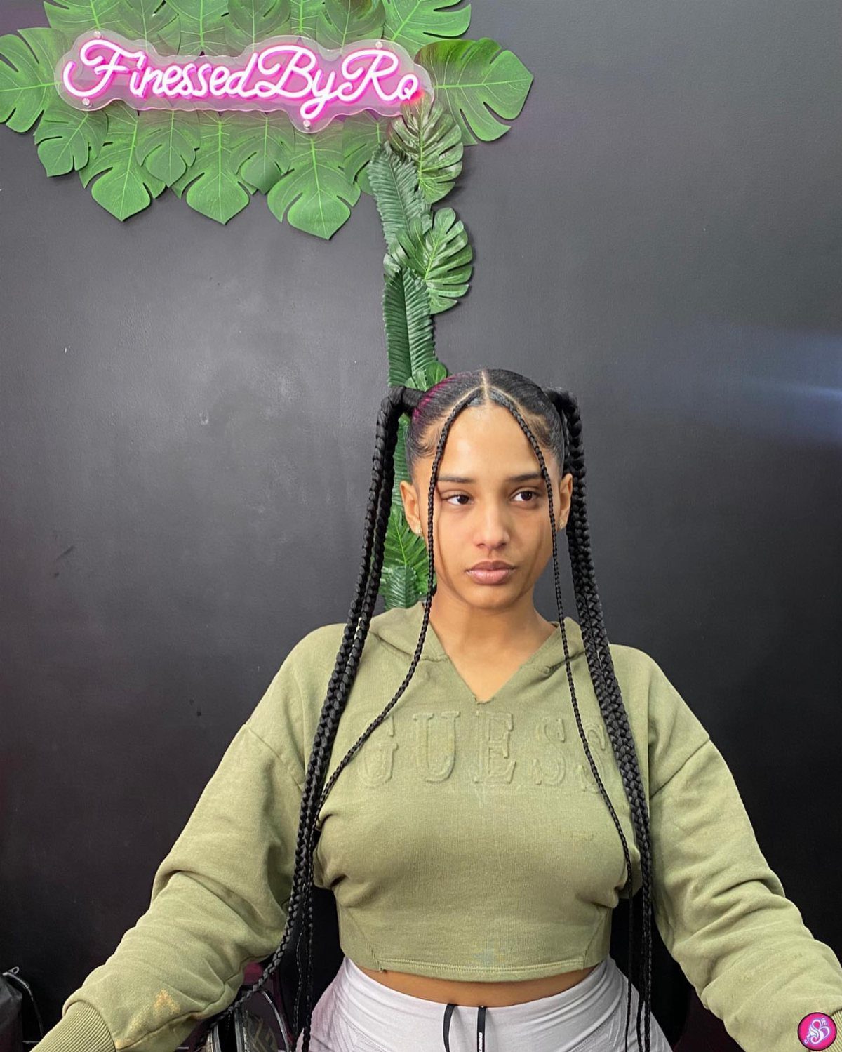 Woman with long black braided pigtails wearing an olive green cropped hoodie.