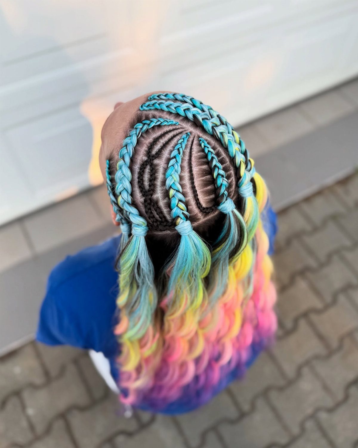 Cornrow braids transitioning into colorful rainbow curly ponytails on a person's head.