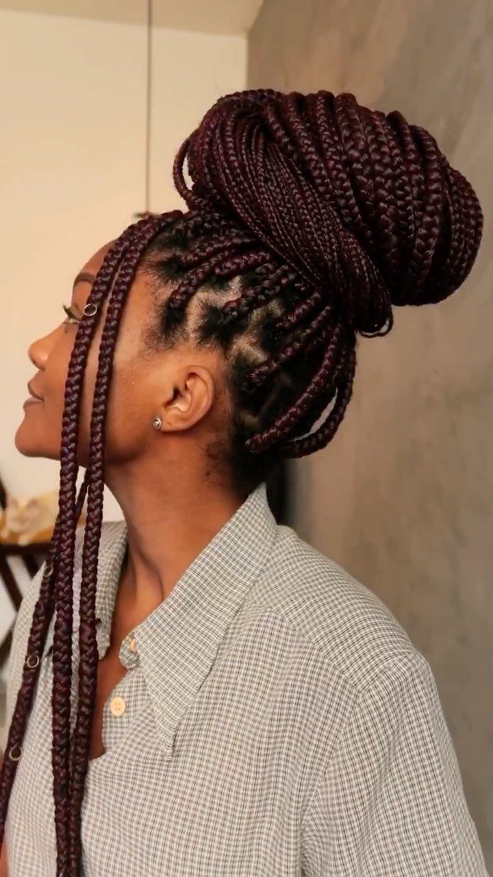Woman with burgundy box braids styled in a high bun and loose strands.