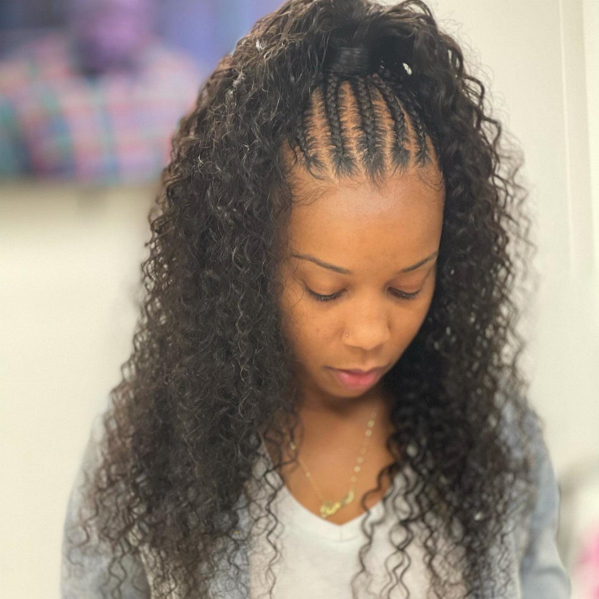 Woman with cornrows on top pulled into a half-up ponytail with loose curly hair.