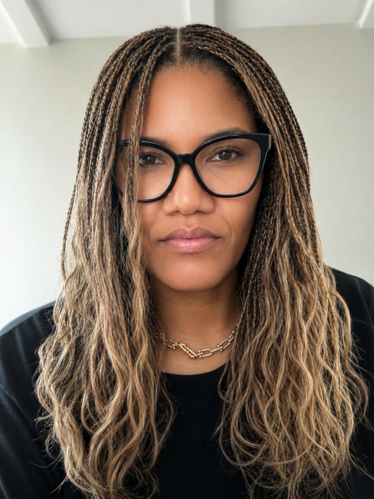 Woman with long, thin brown and blonde micro braids wearing black glasses.
