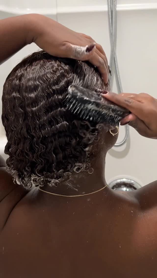 Person applying a white hair mask to curly dark hair with a brush.
