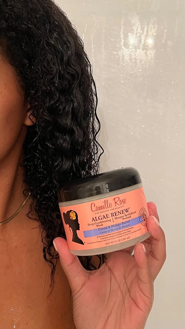 Camille Rose Algae Renew hair mask jar held against dark curly hair.