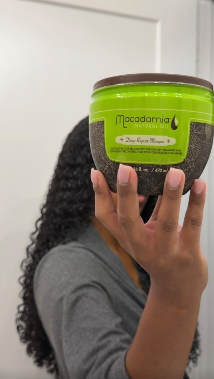 Person with curly hair holding a lime green Macadamia Natural Oil hair mask jar.