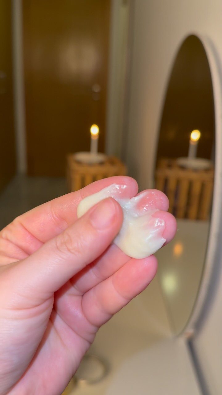 Hand holding a dollop of white hair mask cream with a candle background