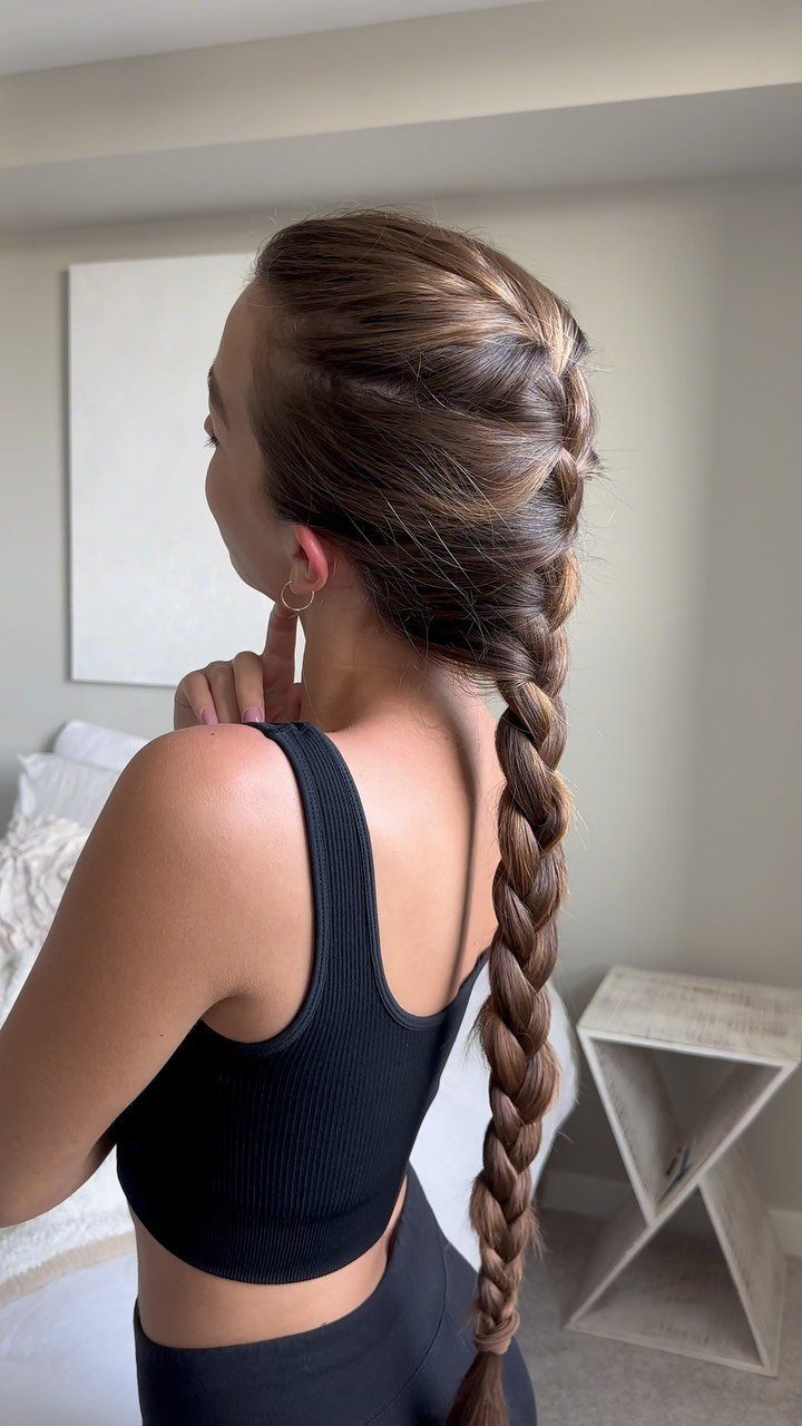 Woman with a long, thick French braid extending down her back in a bedroom.