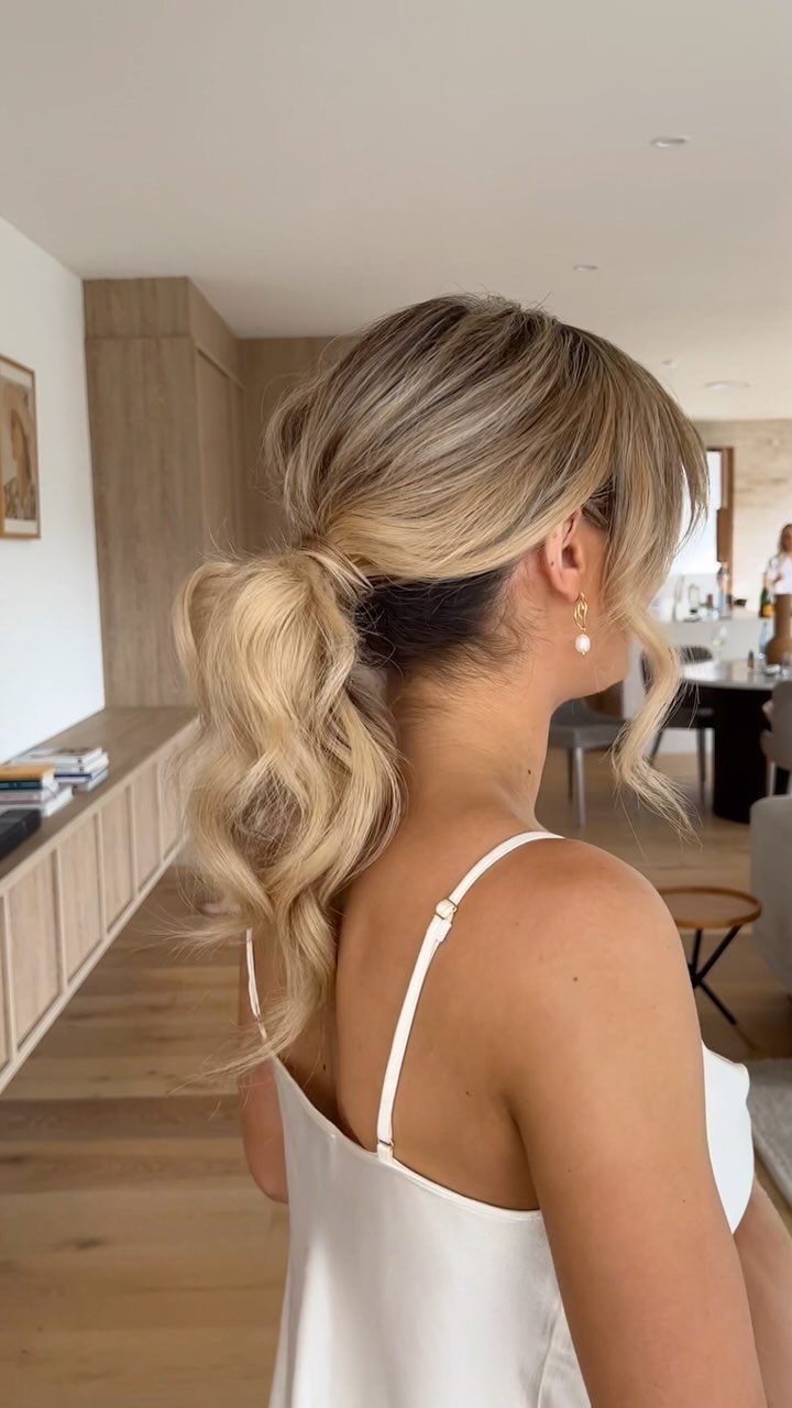Blonde woman with a low, voluminous textured ponytail and loose wavy hair strands.