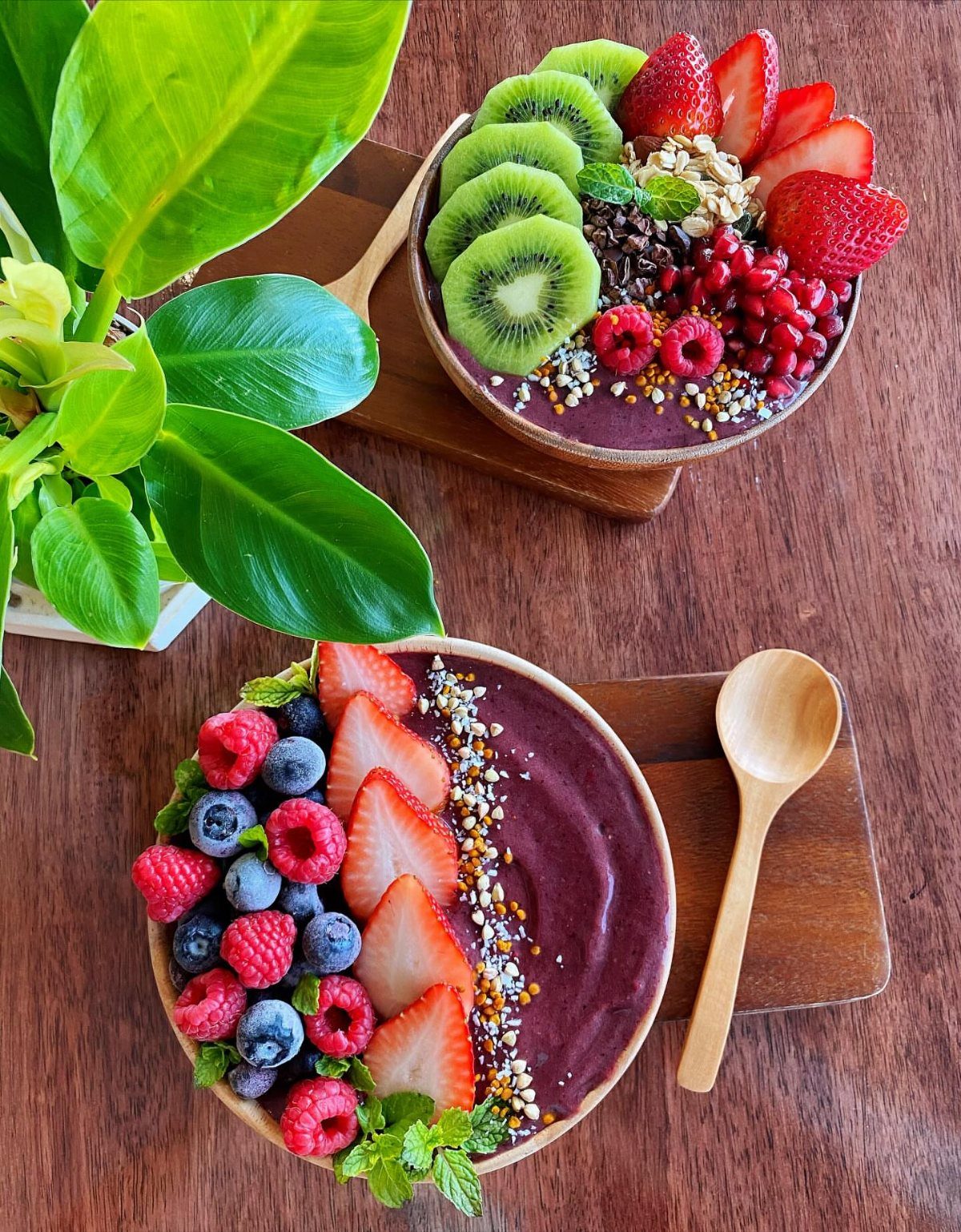 Two purple smoothie bowls topped with fresh strawberries, blueberries, raspberries, and kiwi slices.