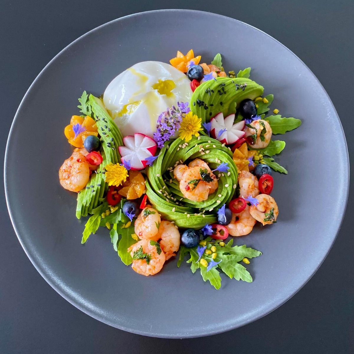 Gourmet plate with avocado, poached egg, shrimp, blueberries, and edible flowers.