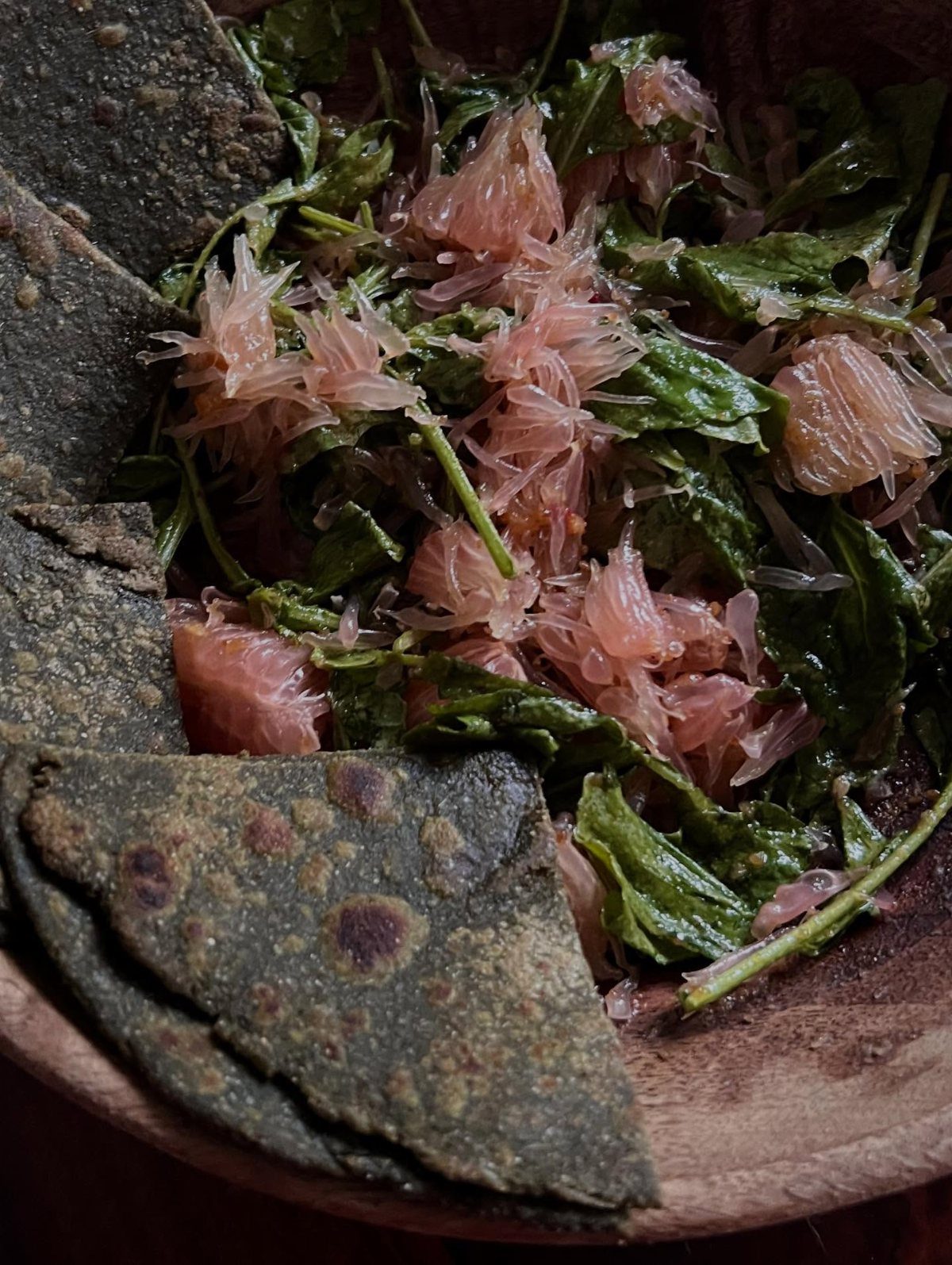 Spinach and grapefruit salad with seed crackers in a wooden bowl.
