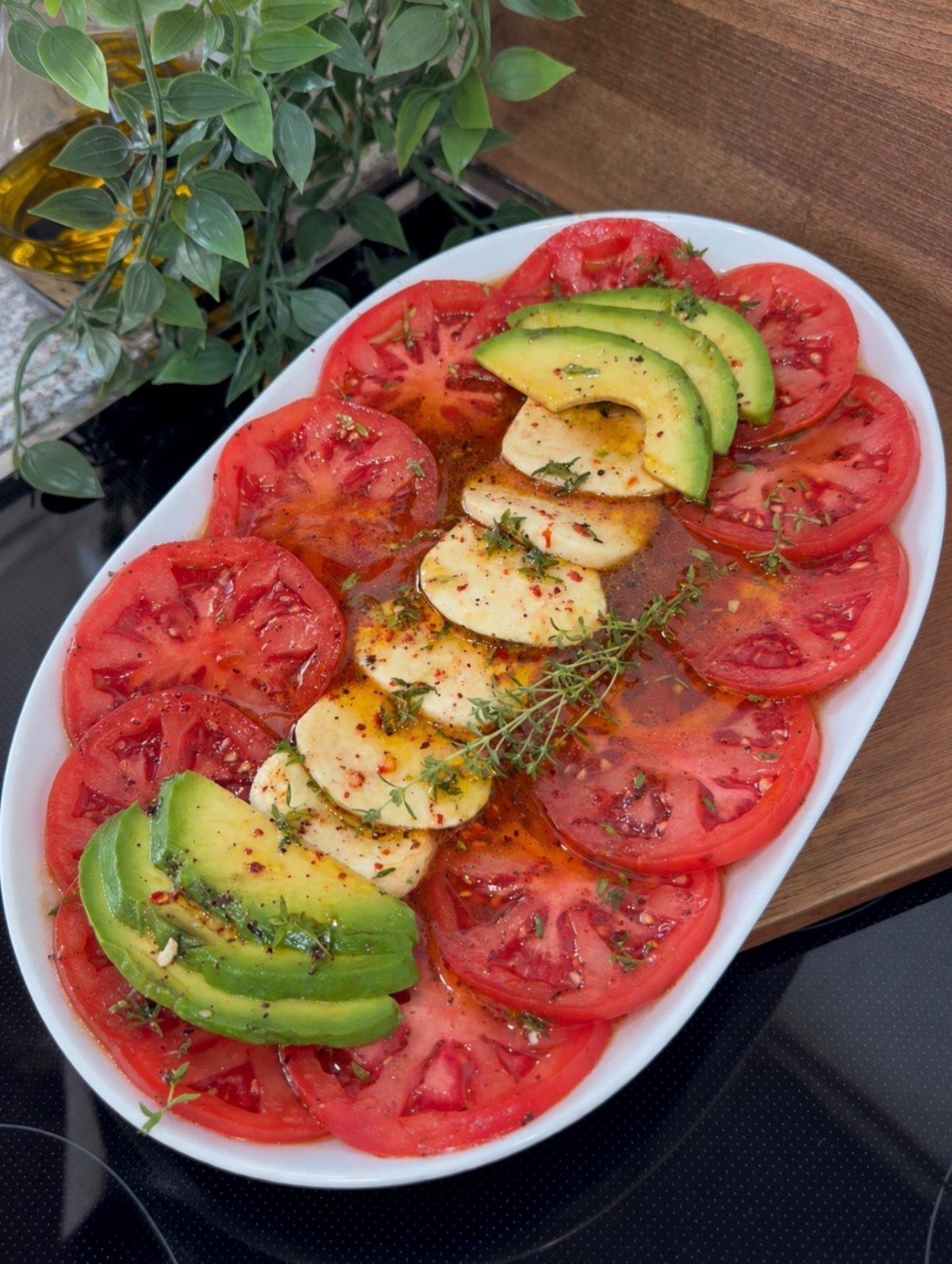 Platter of sliced tomatoes, avocado, and mozzarella cheese seasoned with herbs and oil.