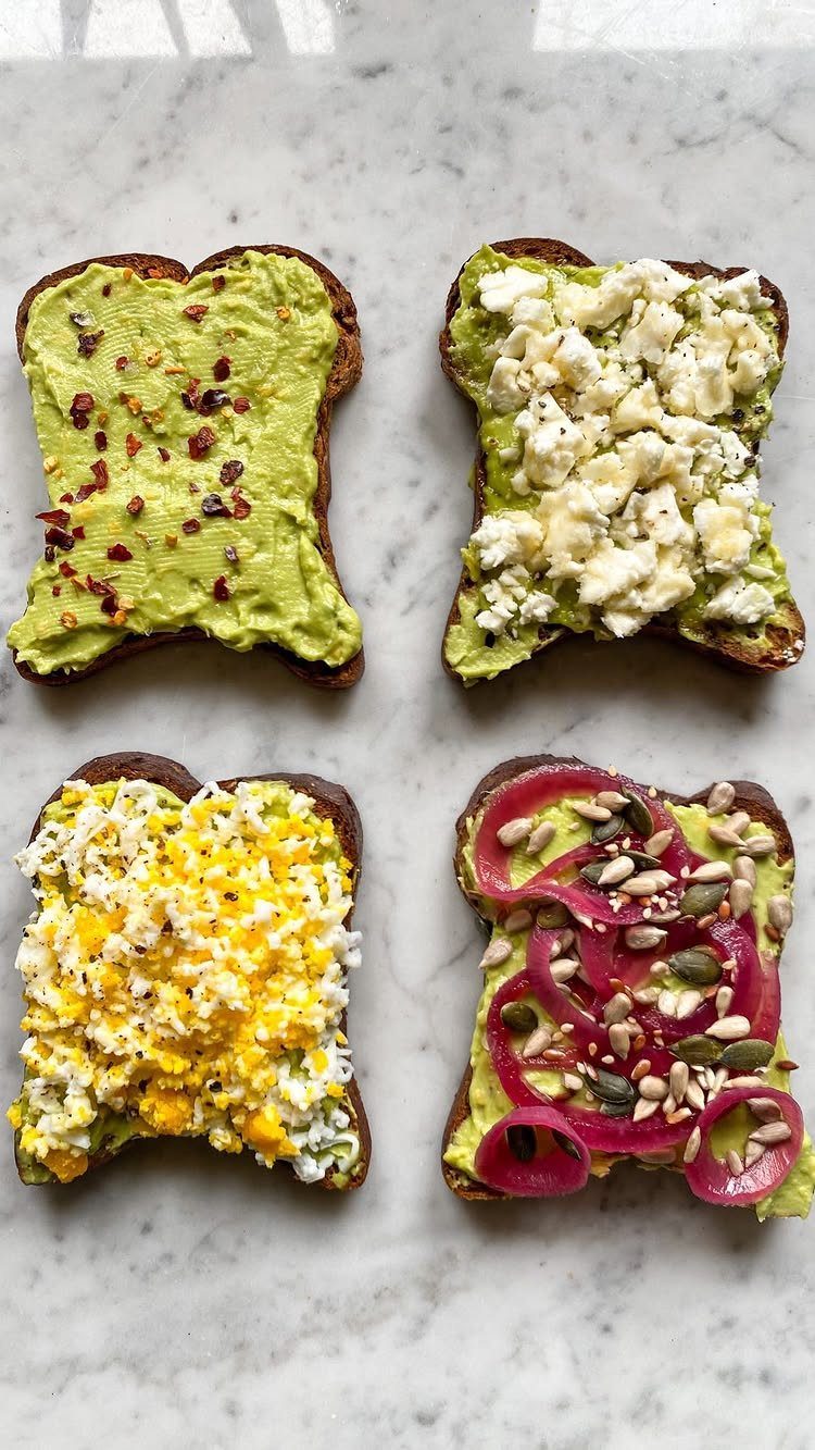 Four avocado toasts with various toppings on a white marble background.