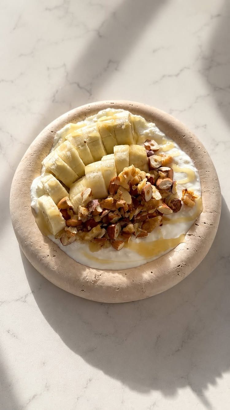 Greek yogurt bowl topped with sliced bananas, chopped nuts, and honey drizzle.