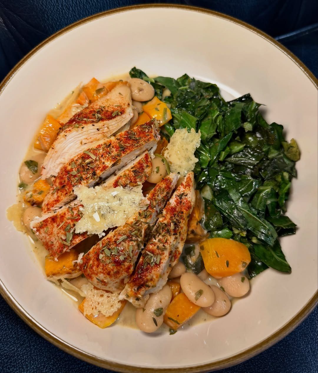 Grilled chicken breast slices with sautéed greens, white beans, and roasted squash in a bowl.