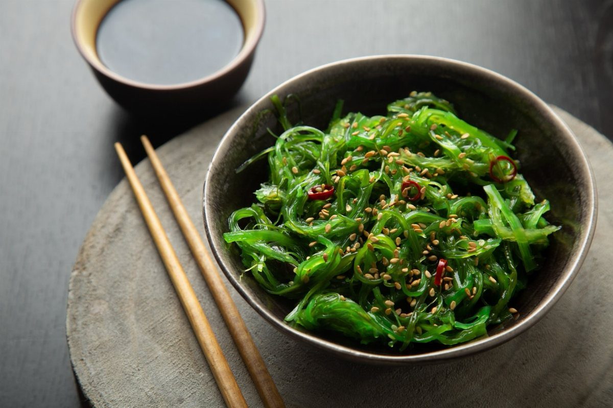 Seaweed salad with sesame seeds and red chili in a dark ceramic bowl.