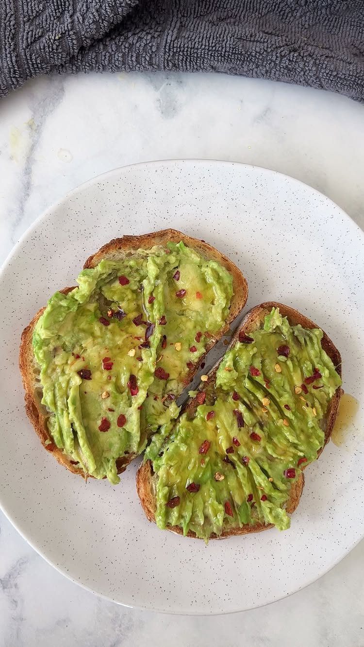 Avocado toast with red pepper flakes on a white speckled plate