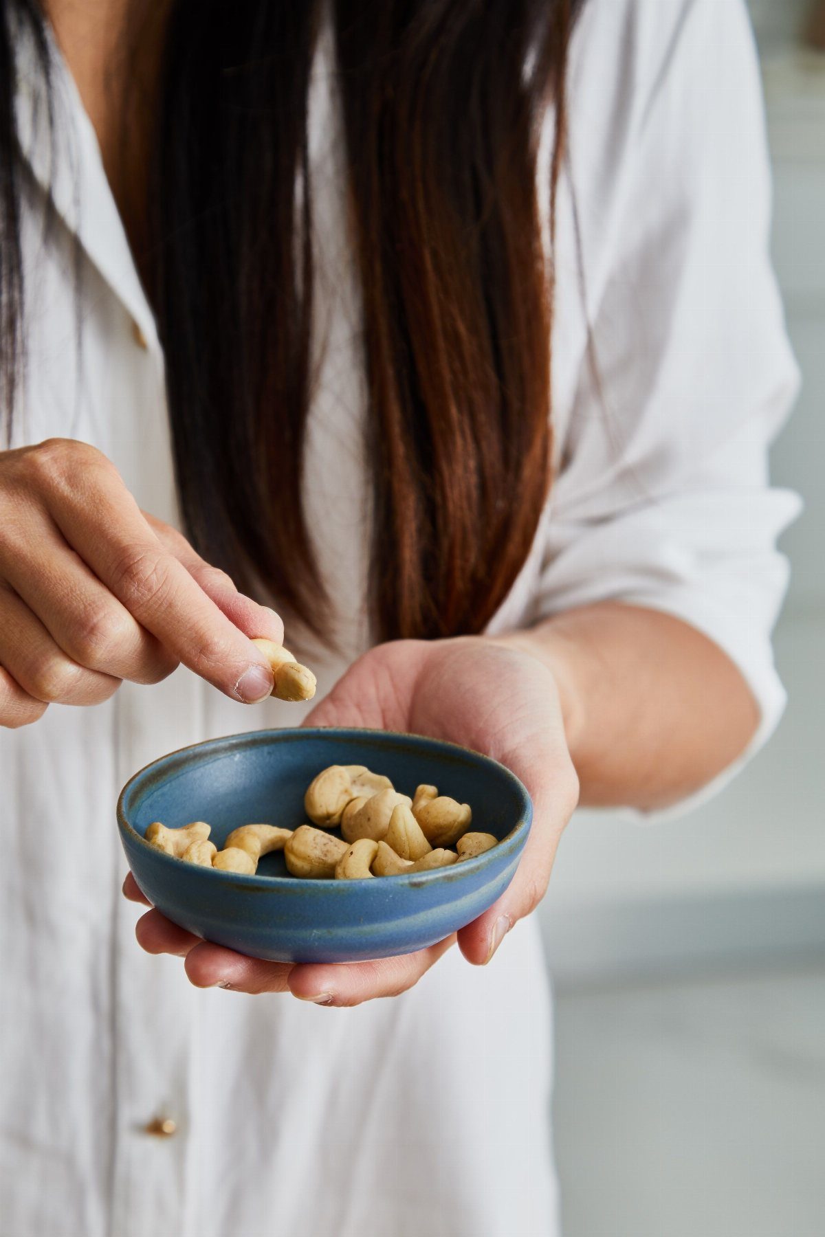 Cashew nuts in a blue bowl held by a person with long hair.