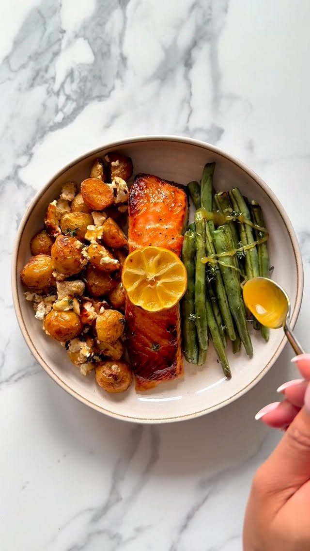 Salmon fillet with roasted potatoes and green beans on a white marble background.