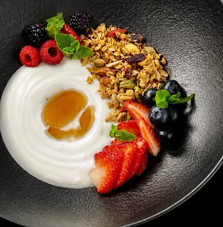 Greek yogurt bowl with honey, granola, and a variety of fresh mixed berries.