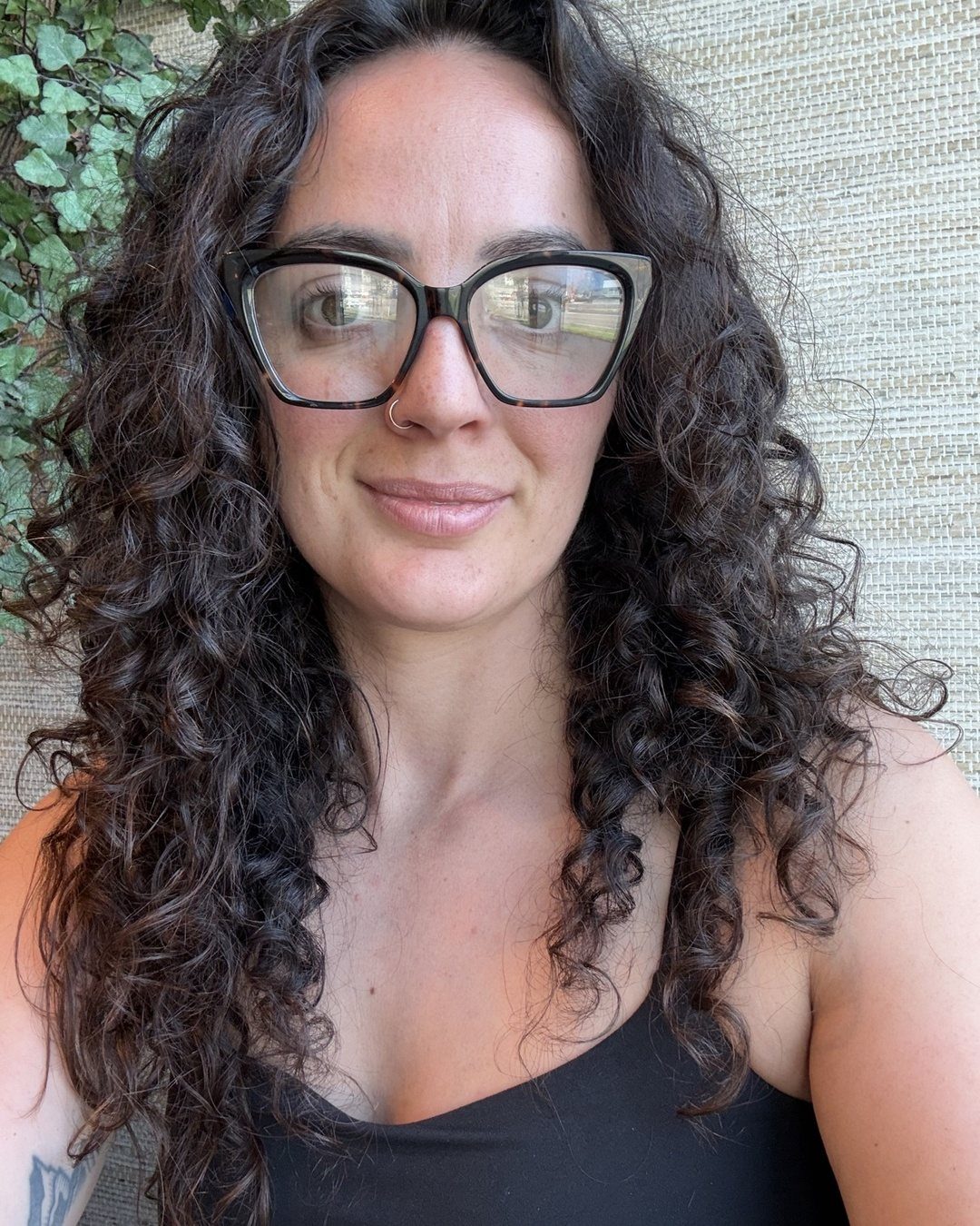 Woman with long dark curly frizzy hair wearing black glasses and black top