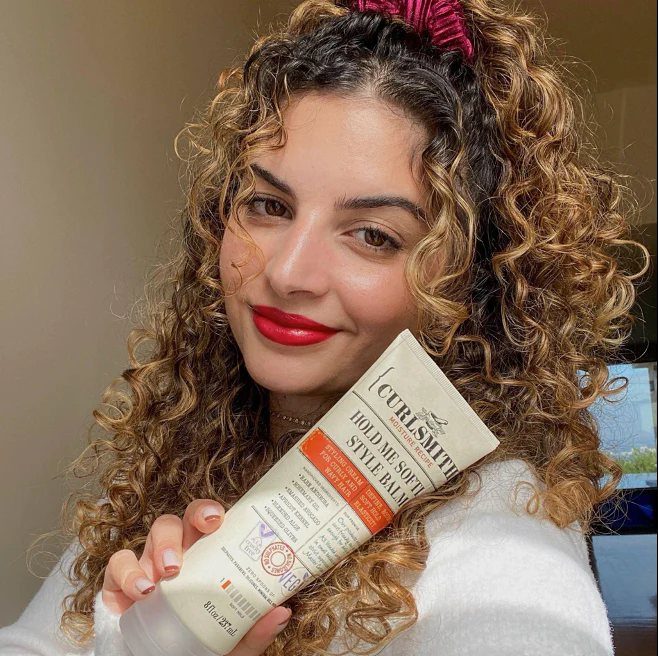 Woman with curly hair holding a tube of curl styling balm