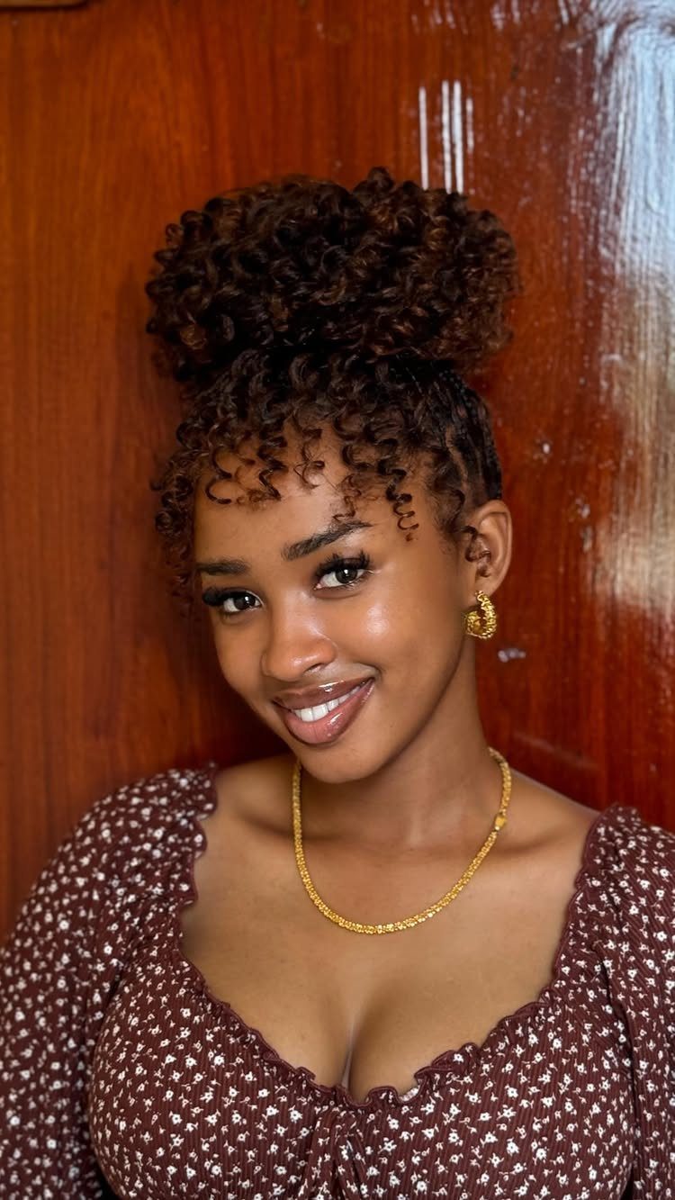 Woman with curly hair styled in a high bun and gold jewelry.