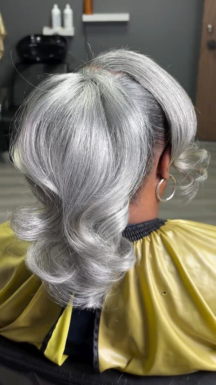Silver and gray hair styled in voluminous soft waves with a yellow salon cape.