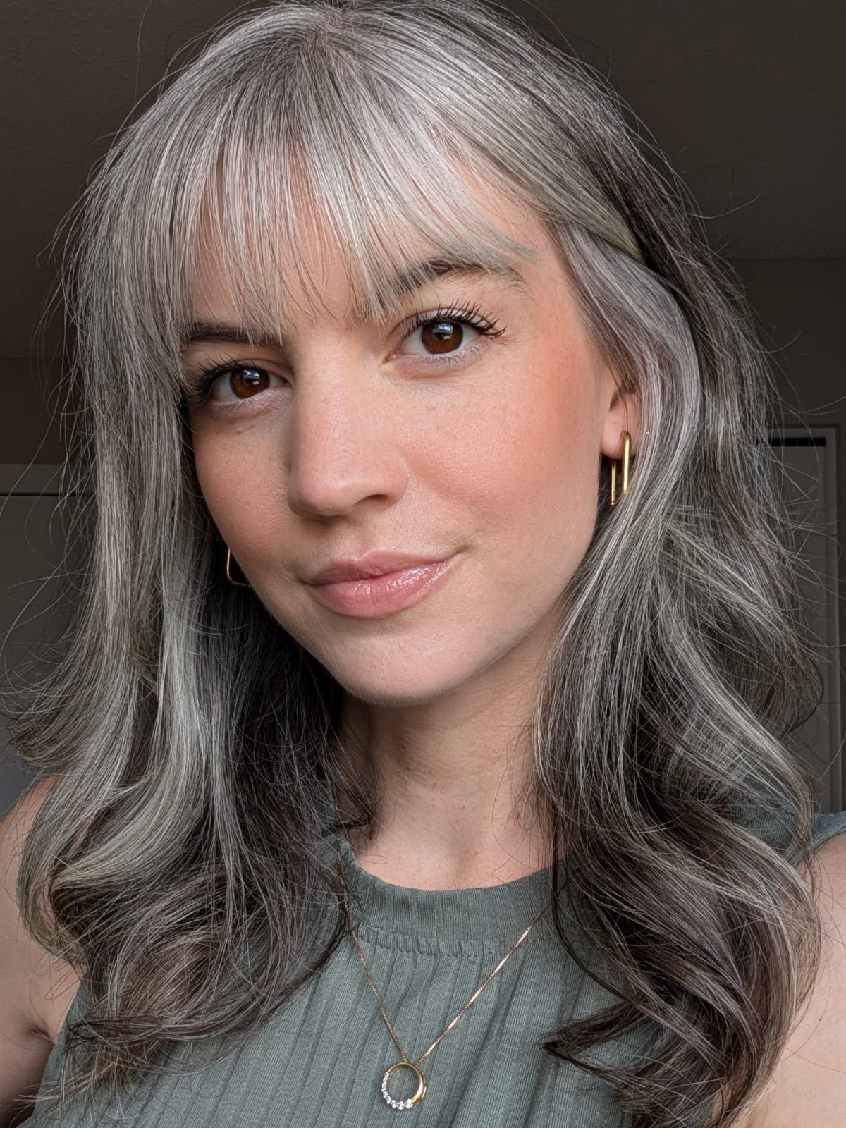 Woman with long soft gray hair and bangs wearing a green top.