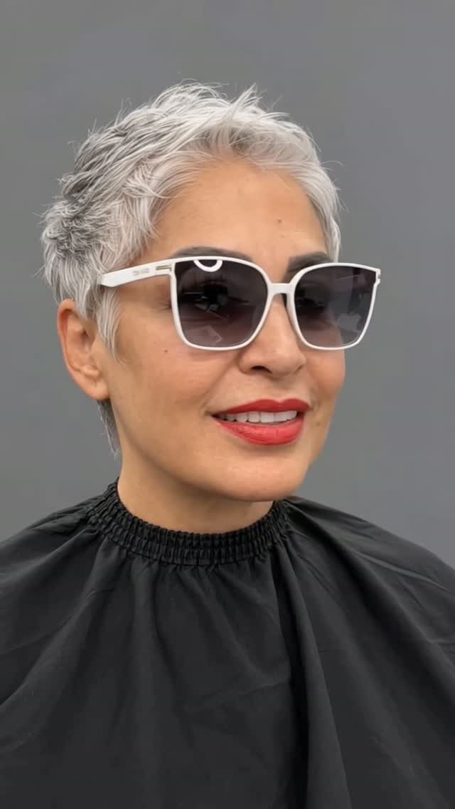 Woman with a short silver-gray pixie haircut wearing white sunglasses and red lipstick.