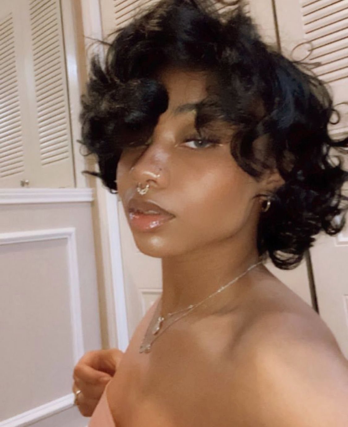 Person with curly grown-out pixie hair and curled bangs posing indoors.