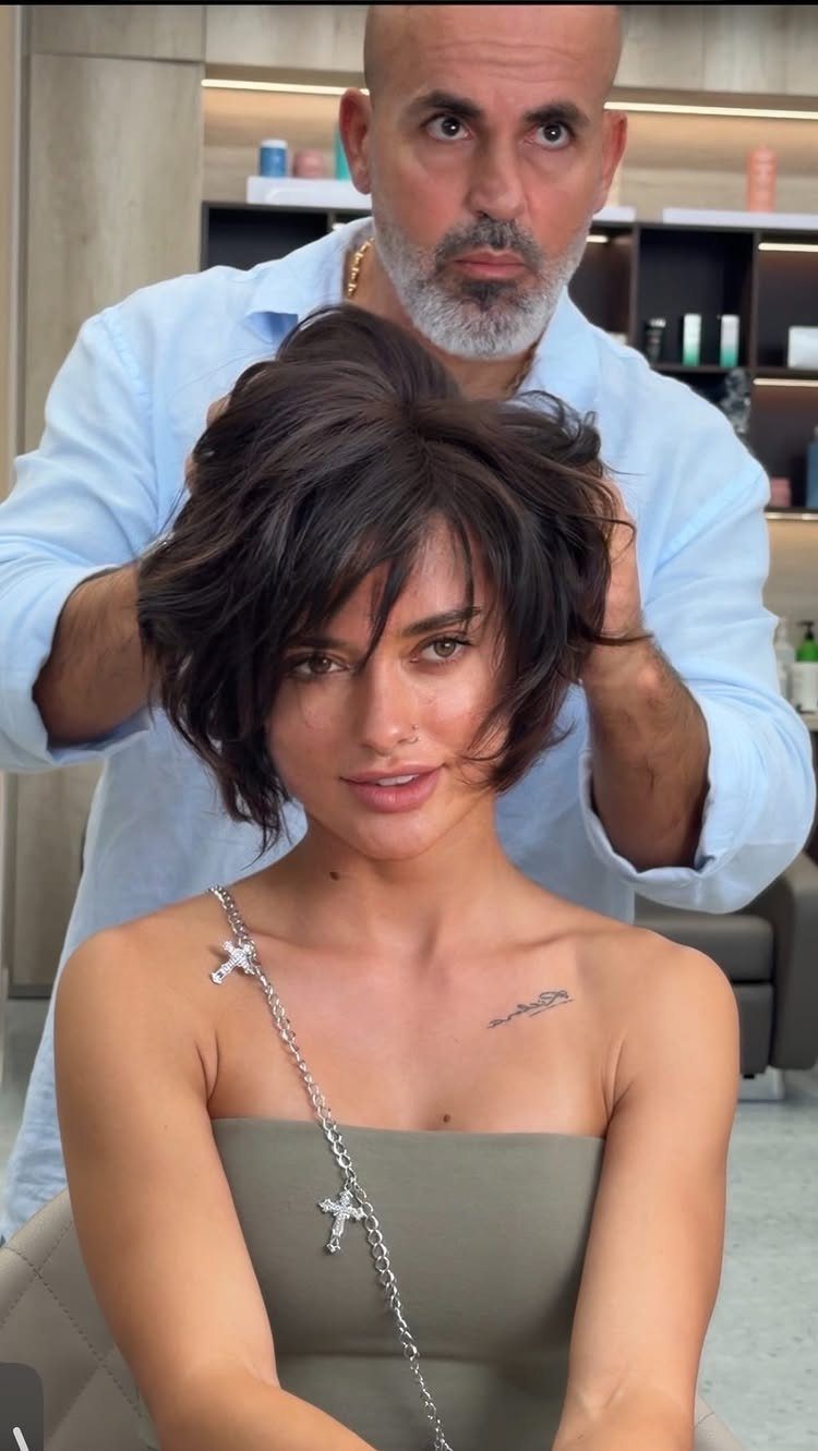 Woman with dark brown feathered layers being styled by a male hairdresser in salon.
