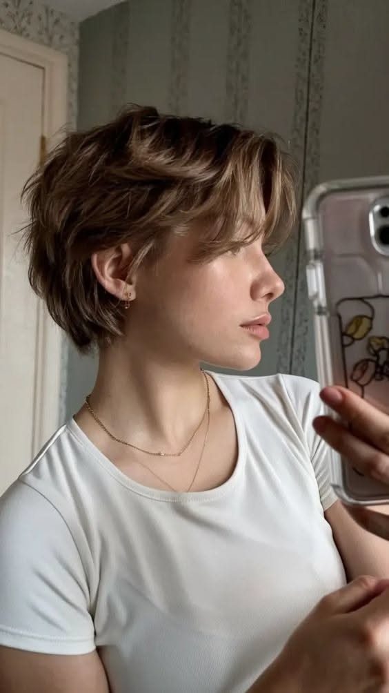 Woman with a light brown grown-out pixie haircut tucked behind her ear.