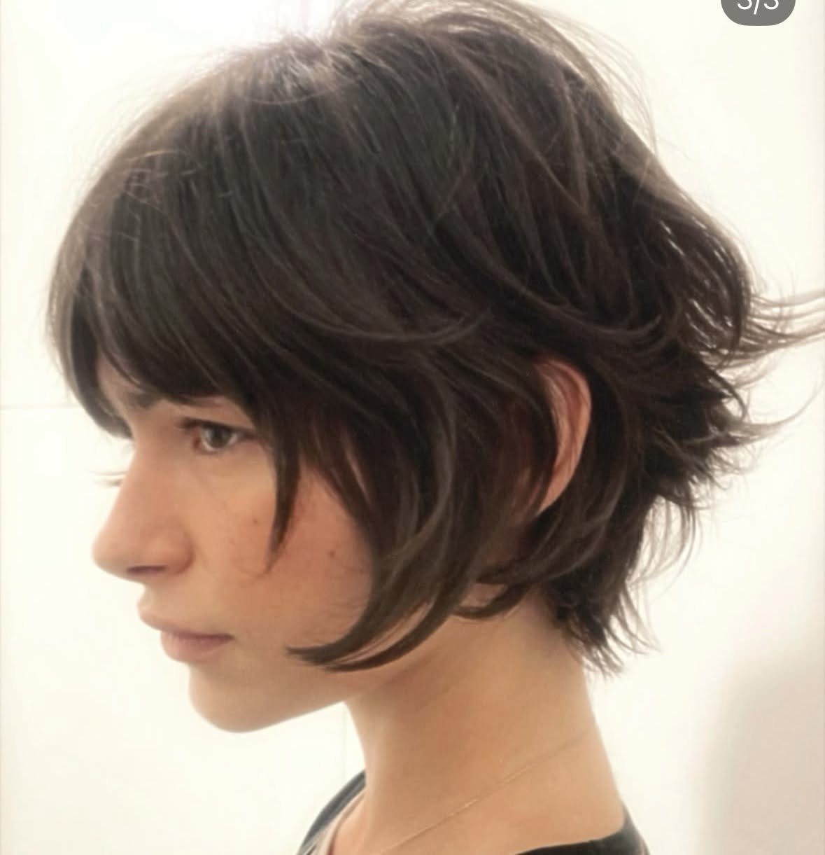 Person with a dark brown textured pixie cut reaching the upper neck length.