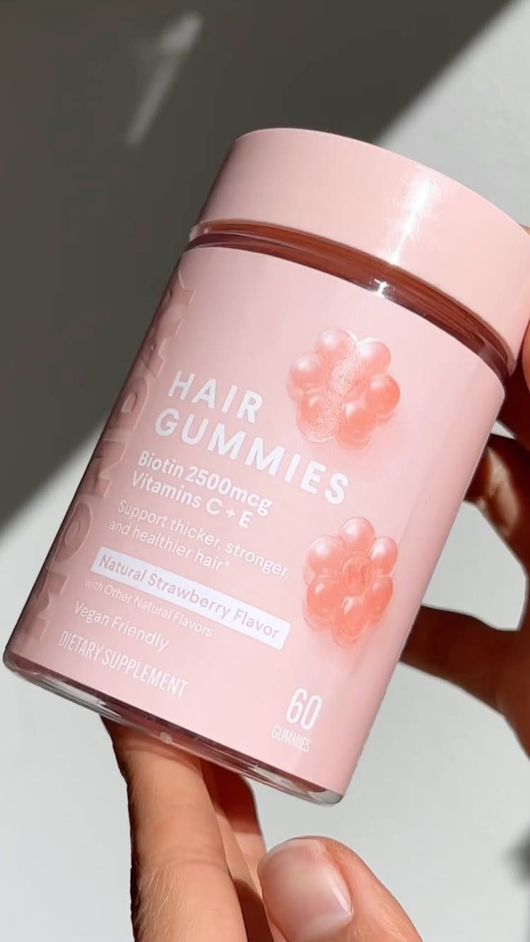 Pink bottle of hair gummies containing biotin held by a person's hand.