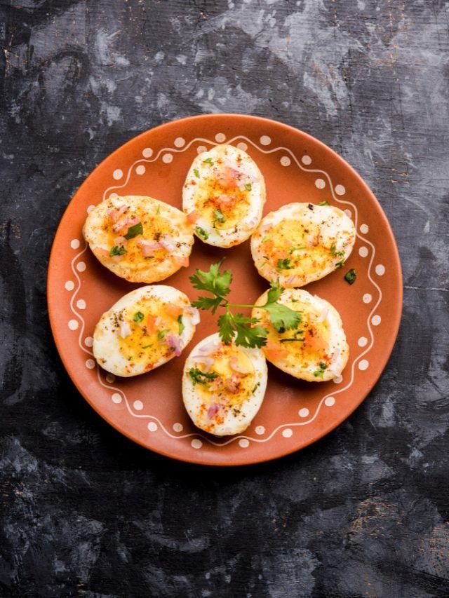 Hard-boiled egg halves with vegetable toppings on a terracotta plate over dark background