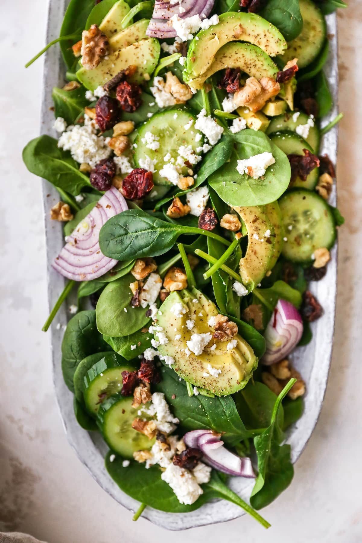 Spinach salad with avocado, cucumber, red onion, feta cheese, walnuts, and dried cranberries.